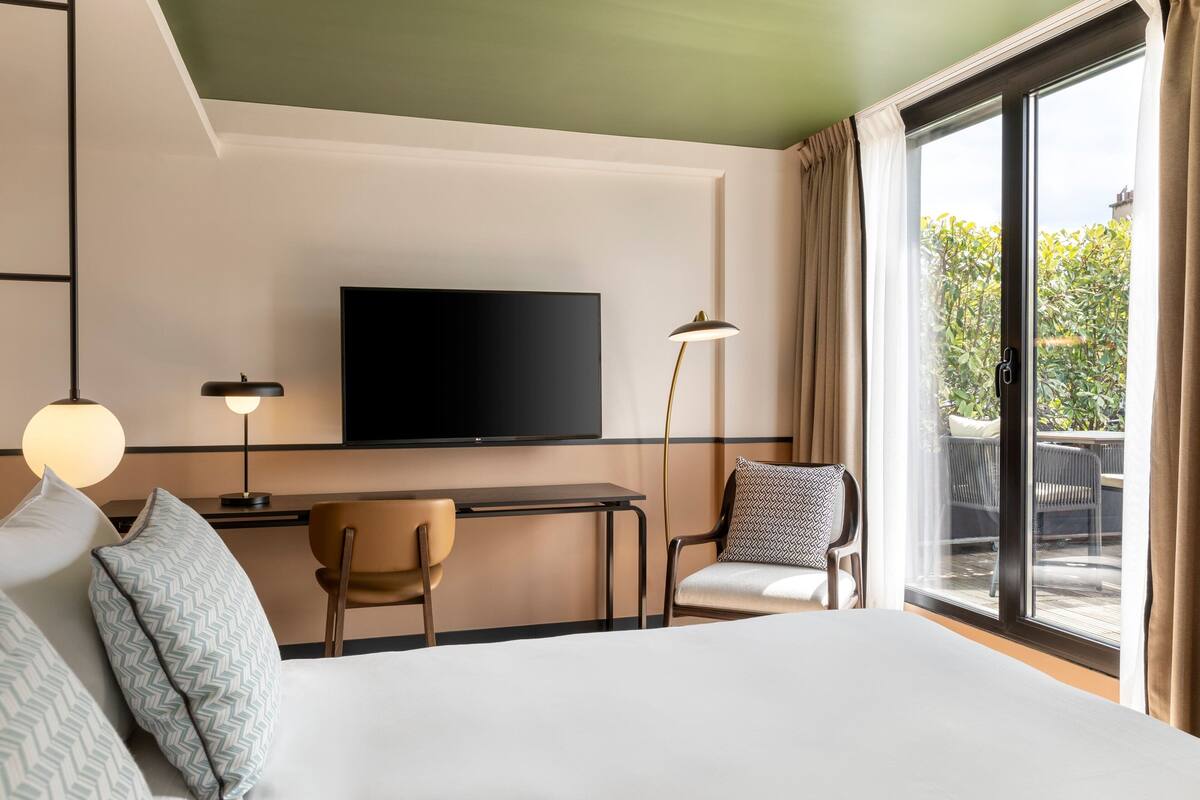 Une chambre d’hôtel équipée d’un lit, d’un bureau, d’une chaise, d’une télévision et offrant une vue sur l’extérieur.