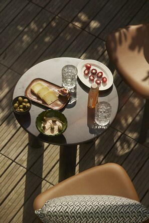 Een ronde tafel met een bord kaas, olijven en een fles water, geplaatst op een houten terras.