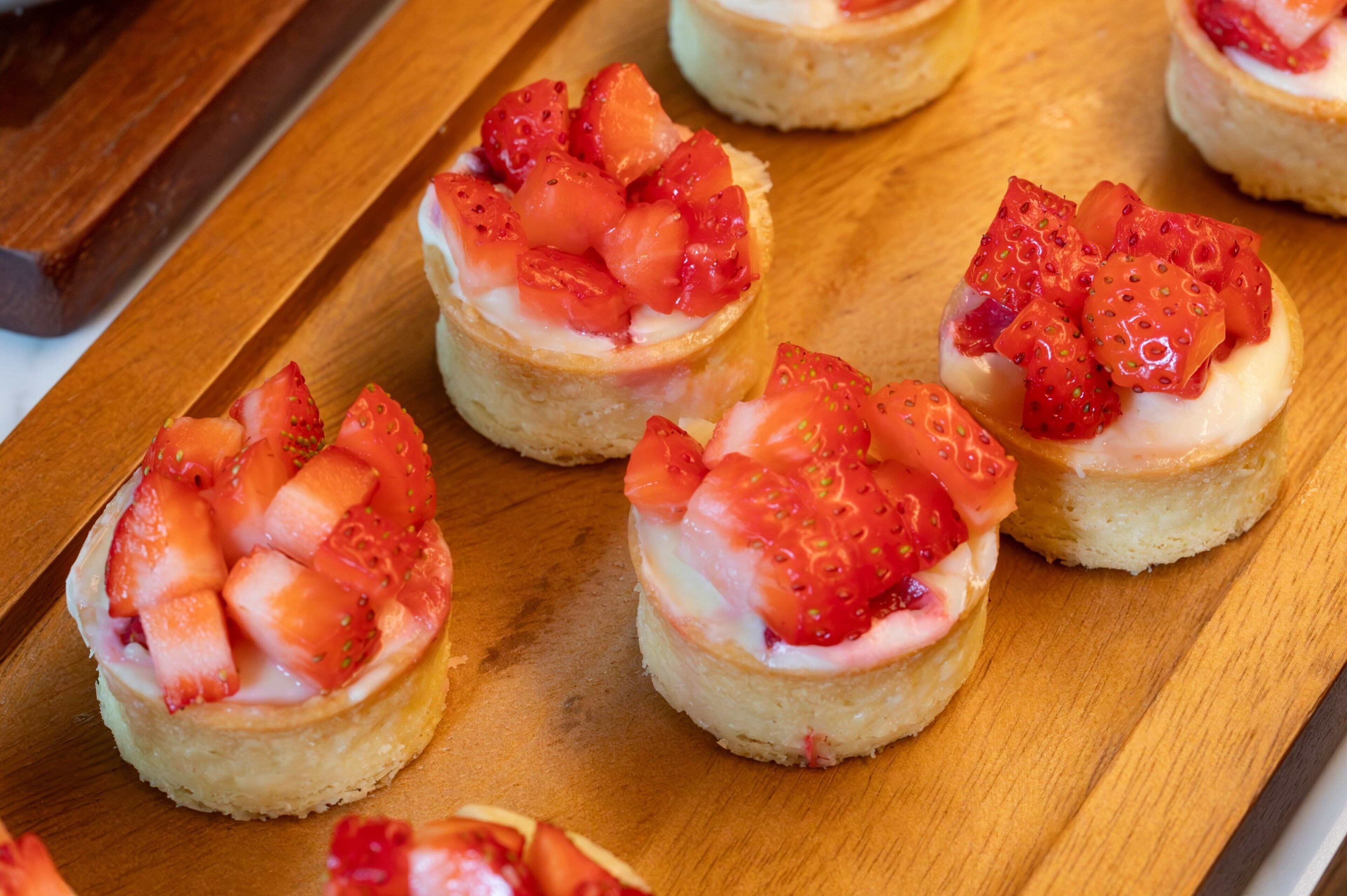 Una tabla de madera con varios pequeños pasteles cubiertos de fresas.