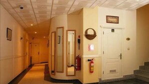 Un couloir d’hôtel avec un extincteur, une porte portant une plaque et un escalier menant à un étage supérieur.