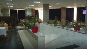 Un grand espace intérieur aménagé avec plusieurs tables et chaises, des plantes en pot et un écran de télévision.