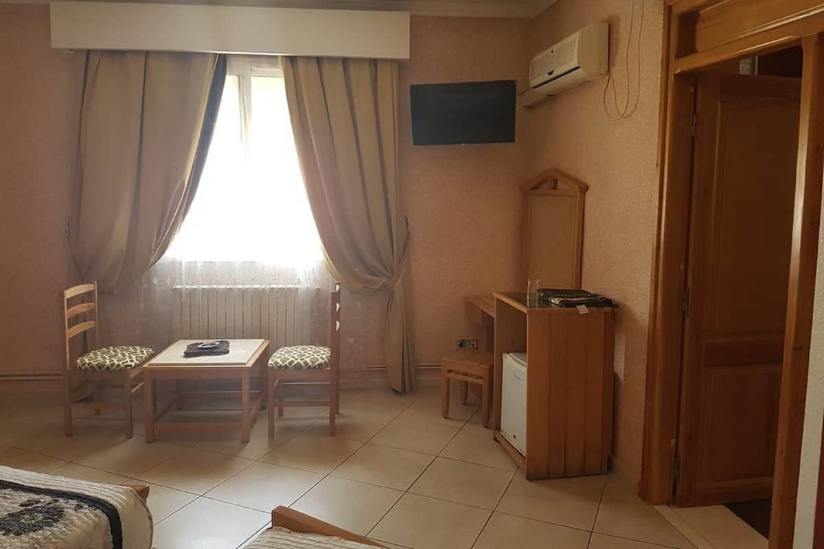 A compact room with a bed, a small table, two chairs, a wooden cabinet, and a window with curtains.