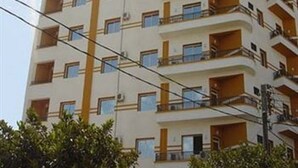 Un immeuble à plusieurs étages doté de balcons, d’un élément vertical central et entouré de verdure.