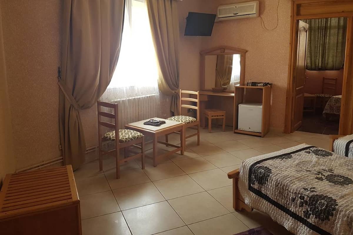 A hotel room with a bed, a desk with a chair, a small table, a mirror, and a television on the wall.
