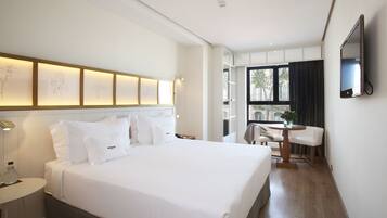 A modern hotel room with a large bed, bedside tables, a desk with a chair, a TV mounted on the wall, and a window with curtains.