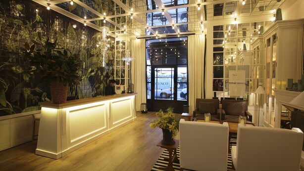 A modern lobby with a reception desk, seating area, and a large window with a view of the street. - Ofelias Hotel (Barcelona)