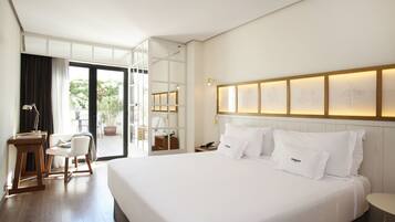 Una habitación de hotel moderna con una cama grande, un escritorio, una silla y un balcón con vistas a zonas verdes.