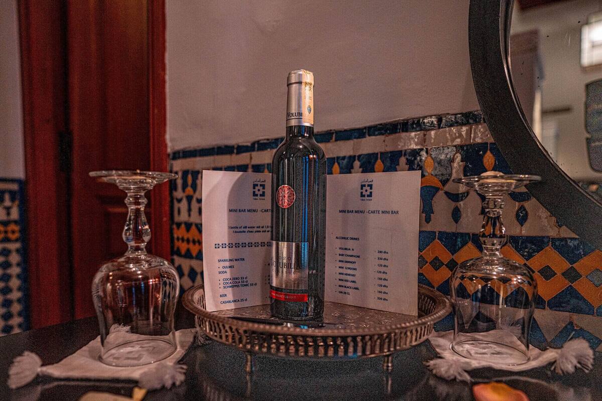 Une bouteille de Volubilia sur un plateau, avec des menus et des verres sur une table.