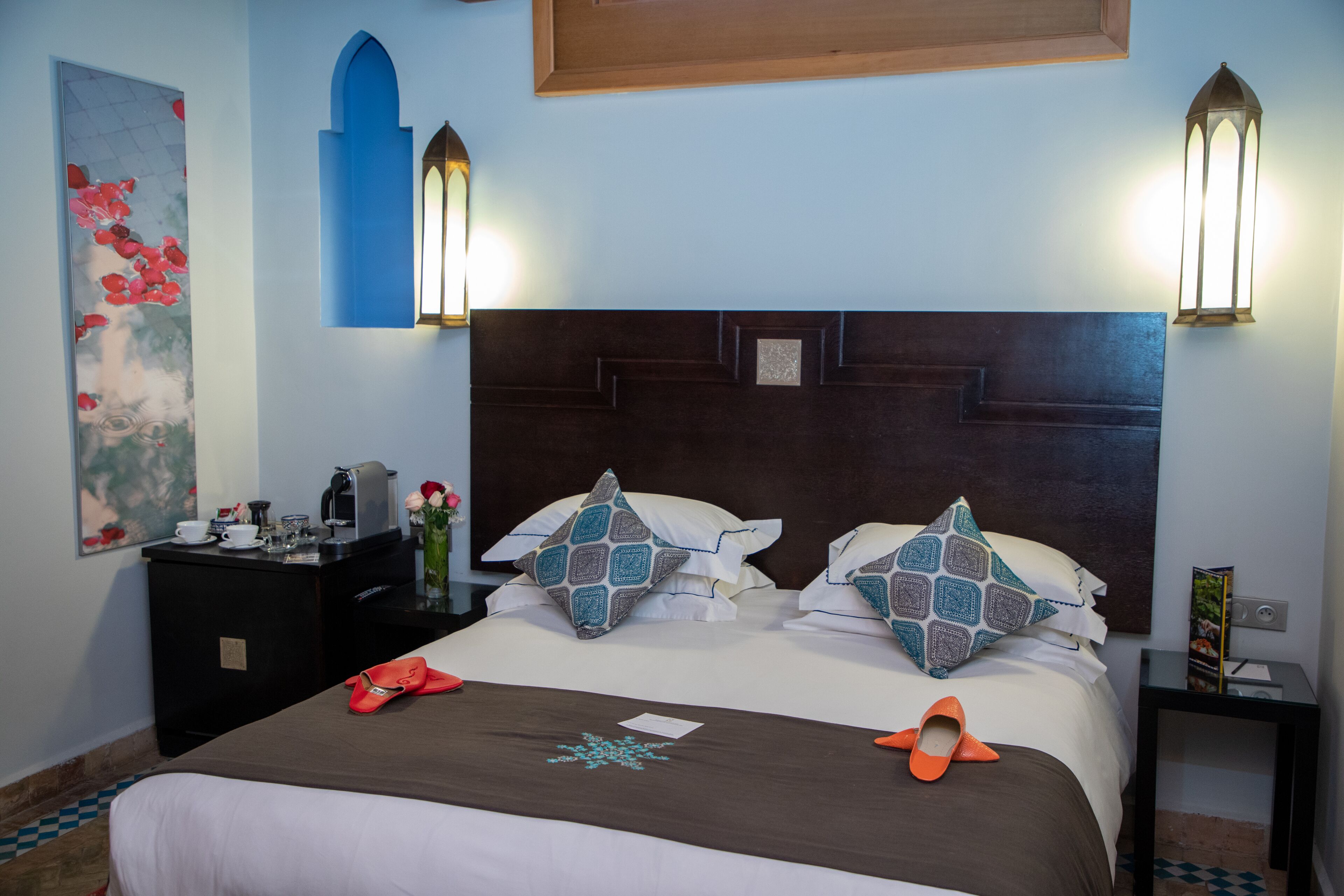Habitación de hotel con una cama grande, dos lámparas de pared, una mesita de noche, un escritorio y un cuadro en la pared.