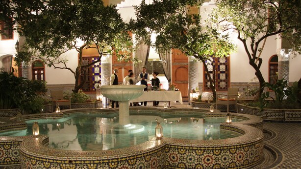 Un patio con una fuente central, rodeado de paredes con azulejos y mobiliario.