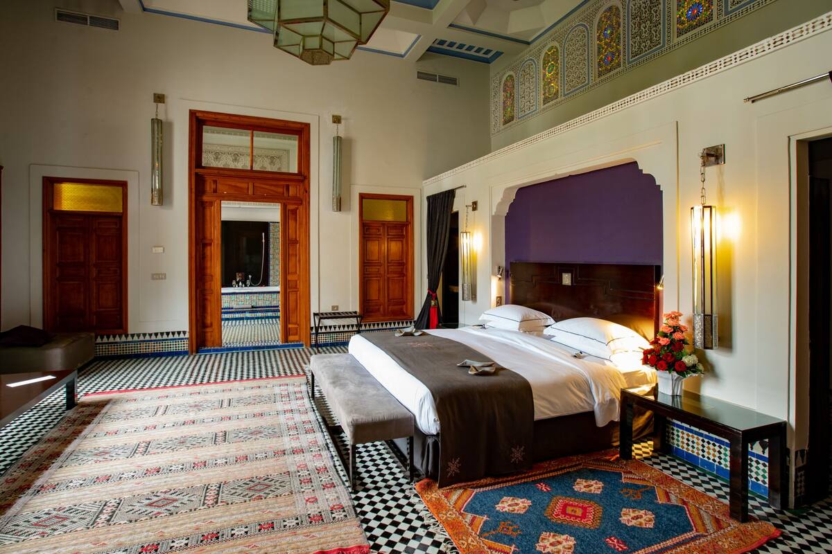 Une chambre spacieuse avec un grand lit, un banc et une salle de bain dont le sol est carrelé.
