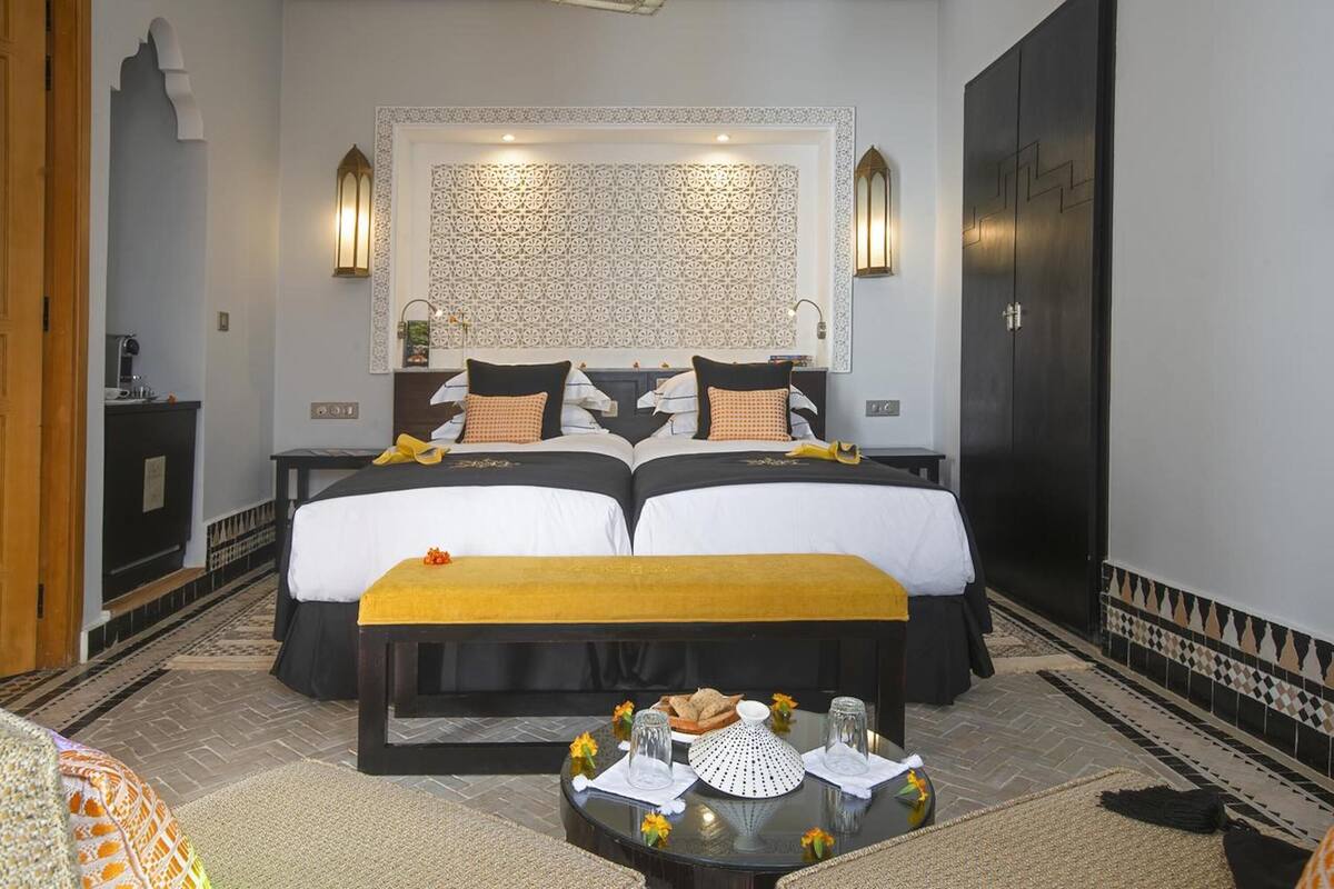 Un lit double avec un couvre-lit jaune, deux tables de chevet, un miroir et un mur décoré d’un motif.