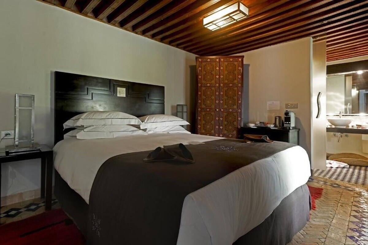 A hotel room with a bed, a nightstand, a wardrobe, a bathroom with a sink, and a mirror.