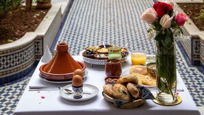 Una mesa de comedor con diversos alimentos y un florero, sobre un piso de baldosas y rodeada de vegetación.