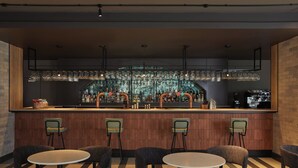 A bar area with a wooden counter, multiple stools, and a hanging light fixture.