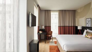 A hotel room with a bed, desk, chair, and a TV mounted on the wall.