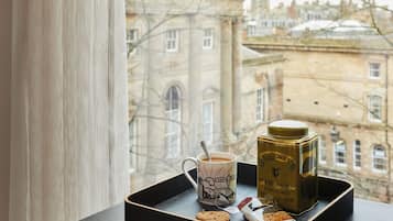 A tray with a mug, a tea tin, and a biscuit on a table by a window overlooking a historic building.