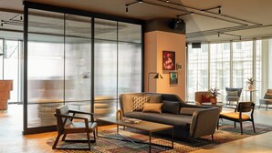 A modern living room with a sofa, armchairs, and a coffee table. There is a large window with blinds, a floor lamp, and a rug.