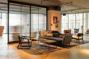 A modern living room with a sofa, armchairs, and a coffee table. There is a large window with blinds, a floor lamp, and a rug.