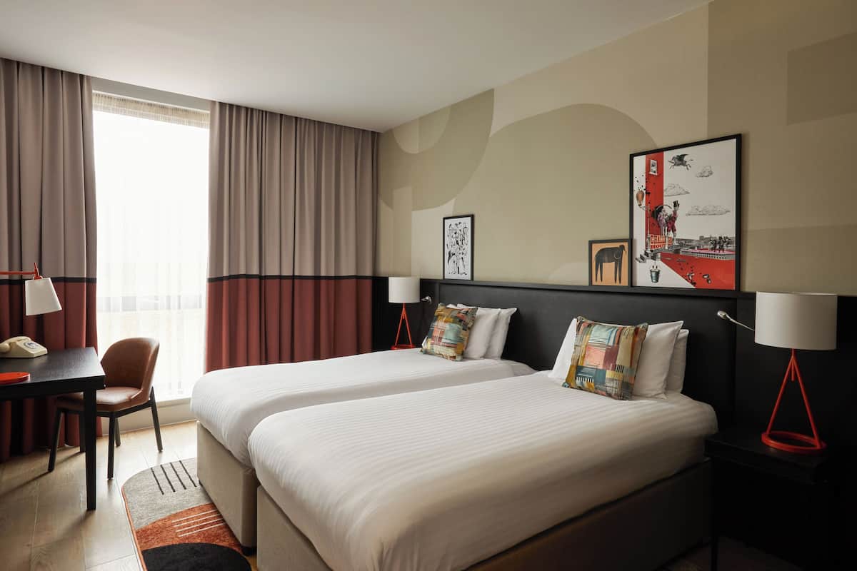 Quarto de hotel com duas camas, uma mesa e uma cadeira.