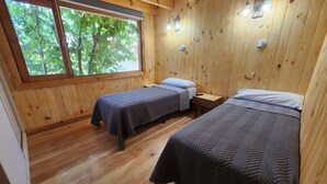 A wooden cabin room with two beds, a window with a view of trees, and wall-mounted lights. - Hosteria Hueney Ruca (San Martín de los Andes)