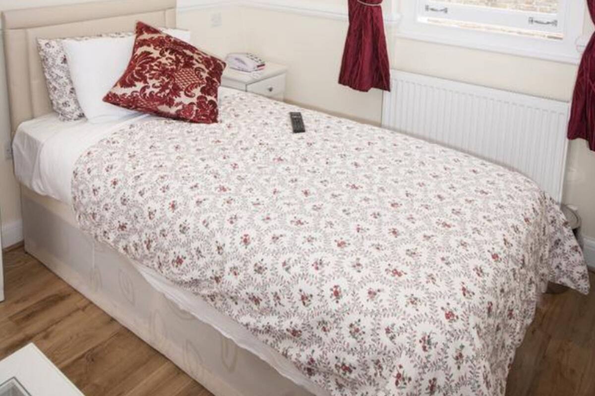 Une chambre à coucher avec un lit, une table de chevet, une fenêtre avec des rideaux et un radiateur.