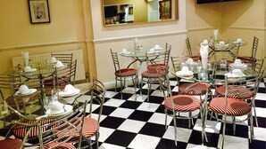 Un espace repas avec des tables en verre et des chaises en métal, un sol à carreaux noirs et blancs et un téléviseur fixé au mur.