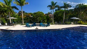 Una piscina con agua azul cristalina, rodeada de sillas de descanso y palmeras.