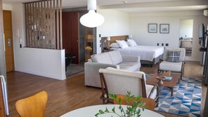 Una habitación de hotel moderna con cama, sofá, sillón y una mesa de comedor con una planta.