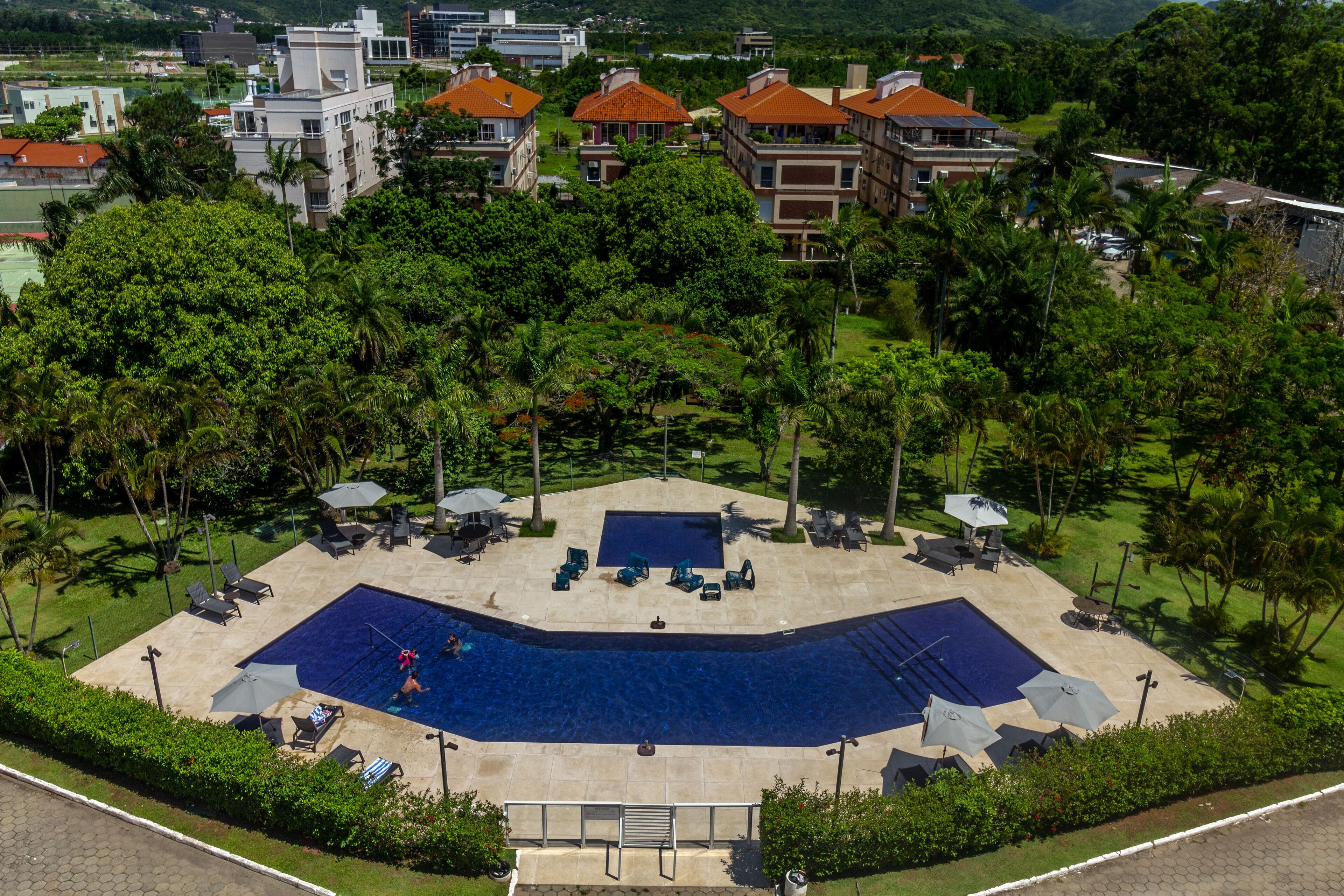 An aerial view of a resort with a large swimming pool surrounded by palm trees and lounge chairs.