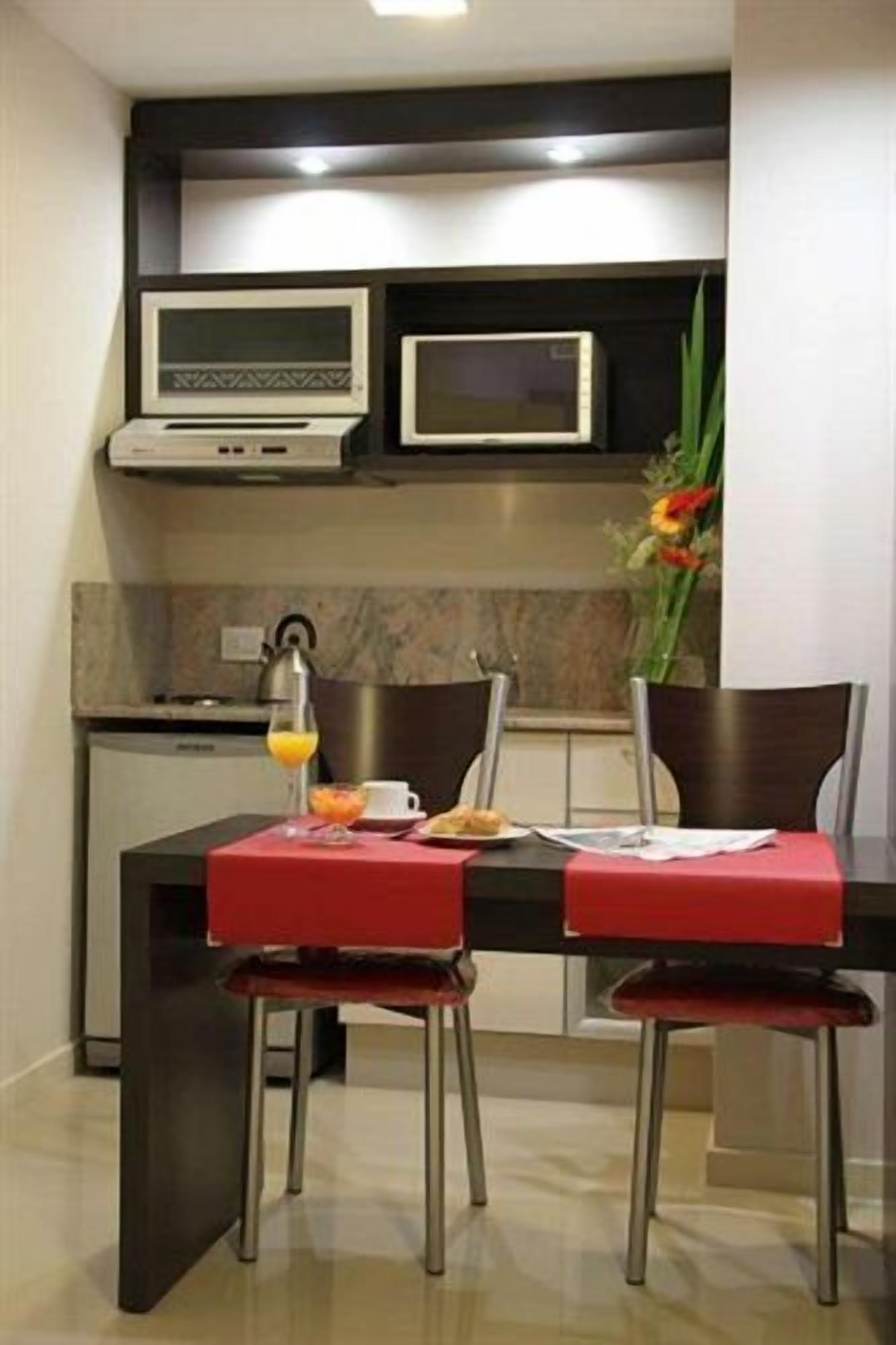 Una cocina moderna con una mesa de comedor, dos sillas, un microondas, una cafetera y un jarrón con flores.