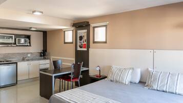 Habitación de hotel con cama, mesita de noche, lámpara y una zona de kitchenette con microondas y cafetera.