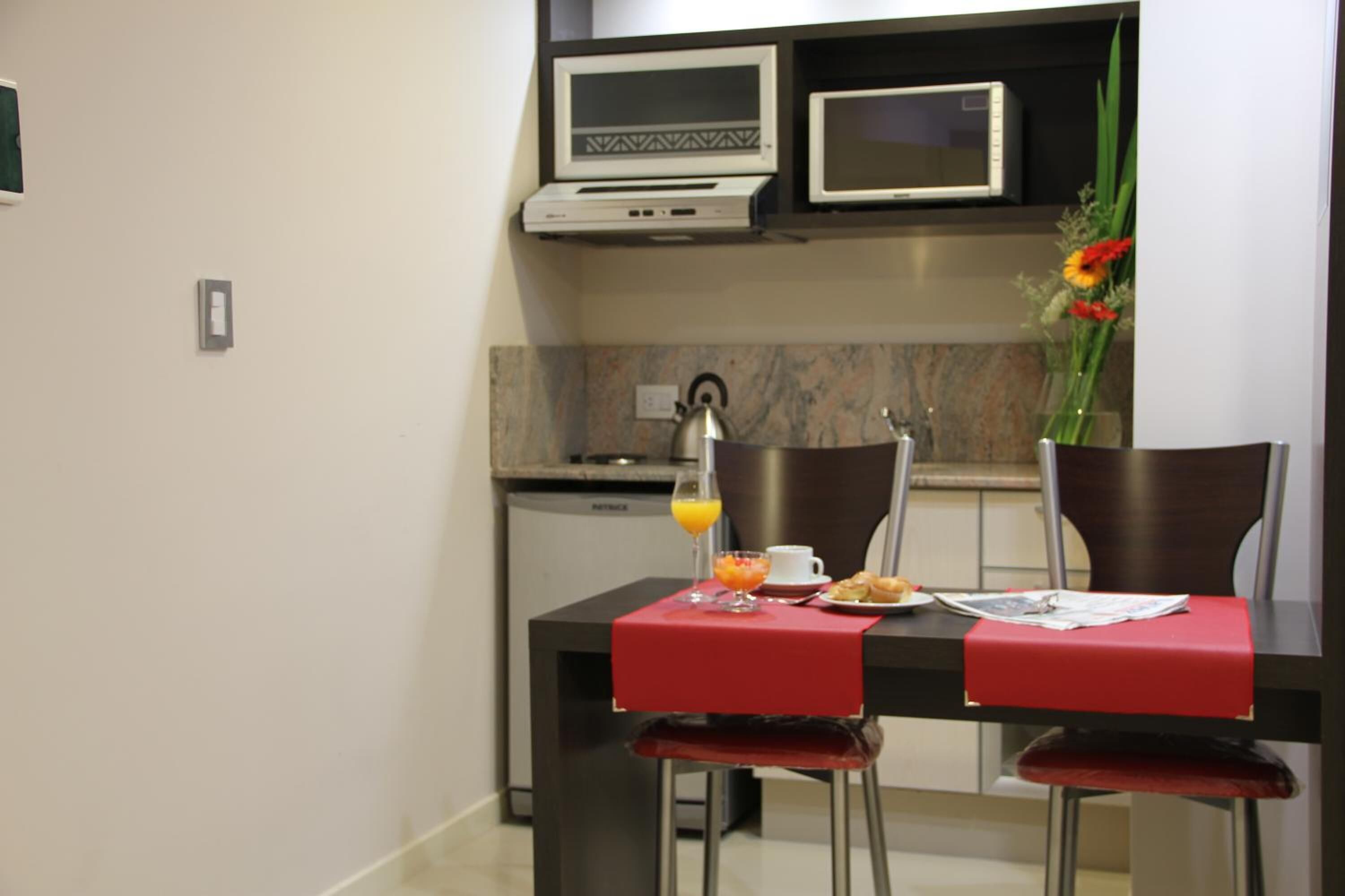 A compact dining area with a table set for two, a coffee cup, a glass of orange juice, and a vase with flowers.