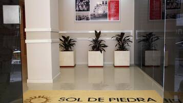 A reception area with a glass partition, potted plants, and a sign reading "SOL DE PIEDRA Apart, Suites & Spa".