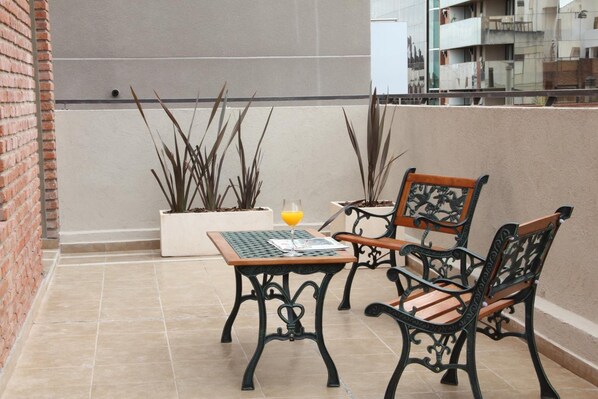 A balcony with a table and two chairs, potted plants, and a glass of orange juice.
