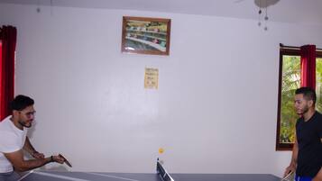 A ping pong table in a room with a ceiling fan, a framed picture on the wall, and a window with curtains.