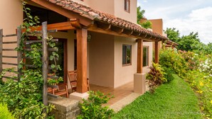 Una casa con techo de tejas, porche cubierto y jardín con diversas plantas.