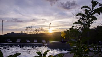 A pool with lounge chairs and a sunset in the background.
