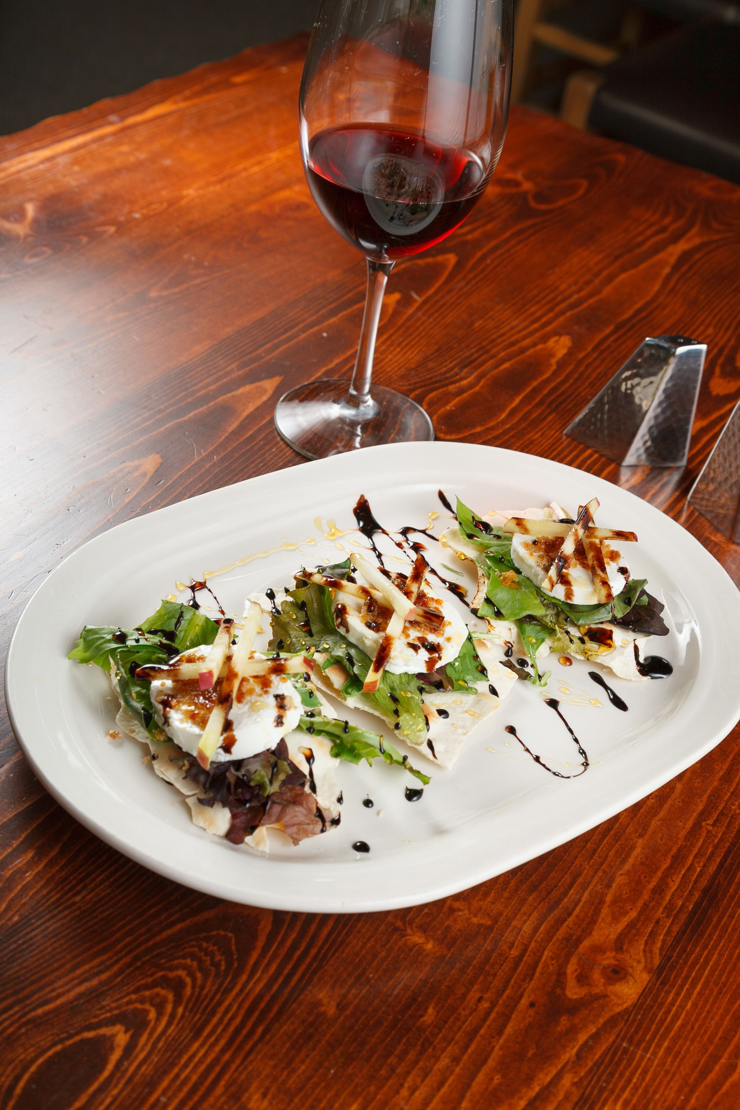 A plate of food on a wooden table with a glass of red wine.