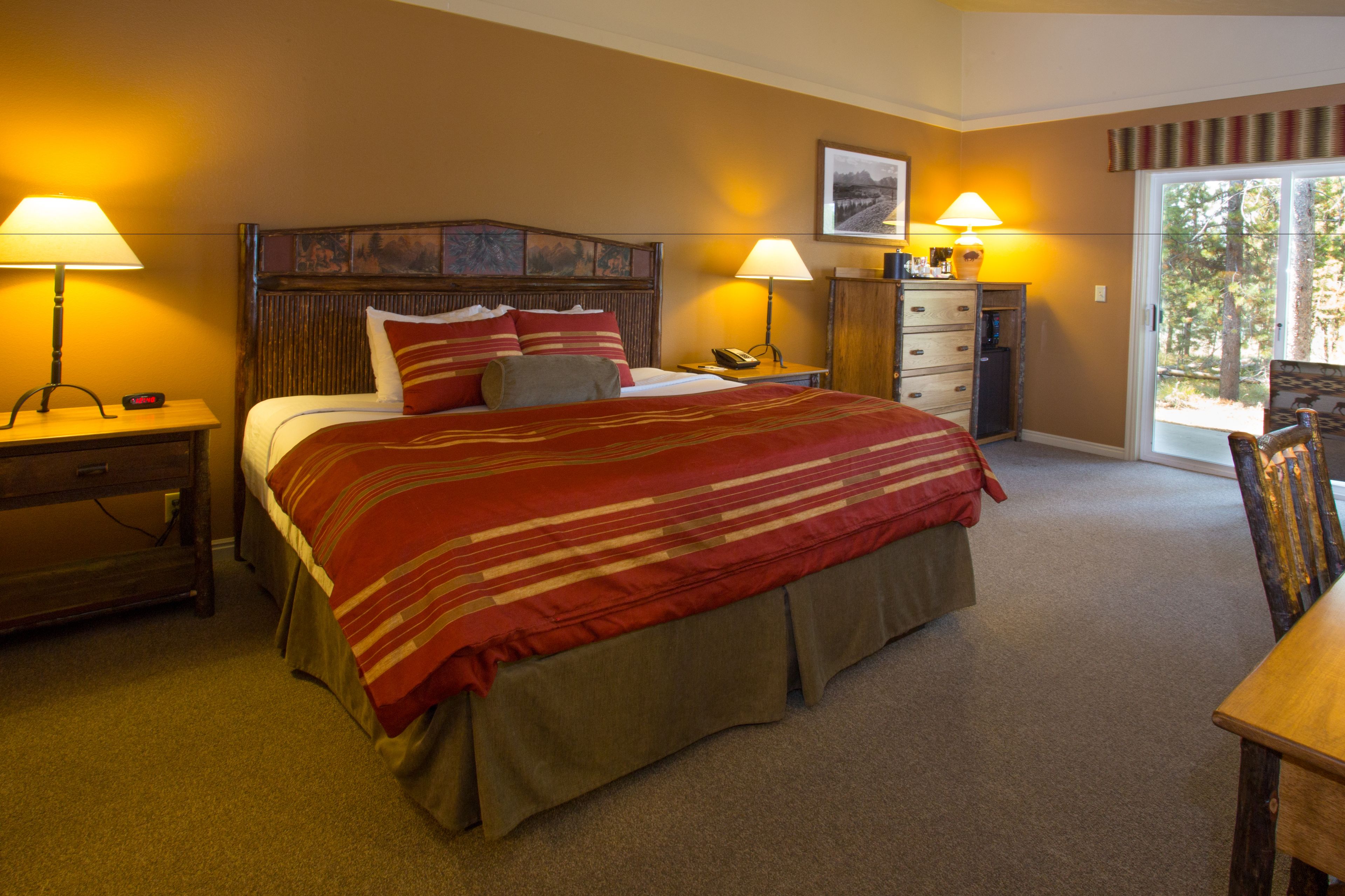 A hotel room with a large bed, two bedside tables with lamps, a wooden headboard, a nightstand, a dresser, and a chair.