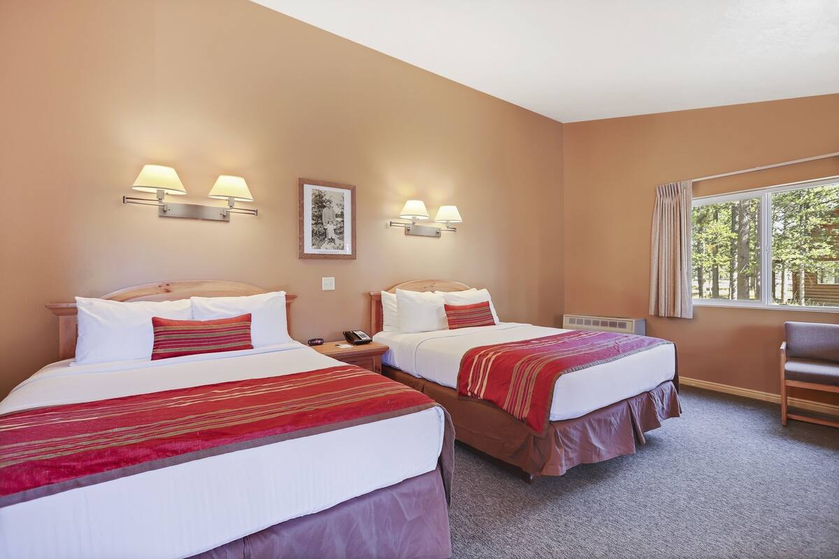 Une chambre d’hôtel avec deux lits, chacun recouvert d’une couvre-lit rouge et blanche, deux appliques murales, un tableau encadré au mur et une fenêtre avec des rideaux.