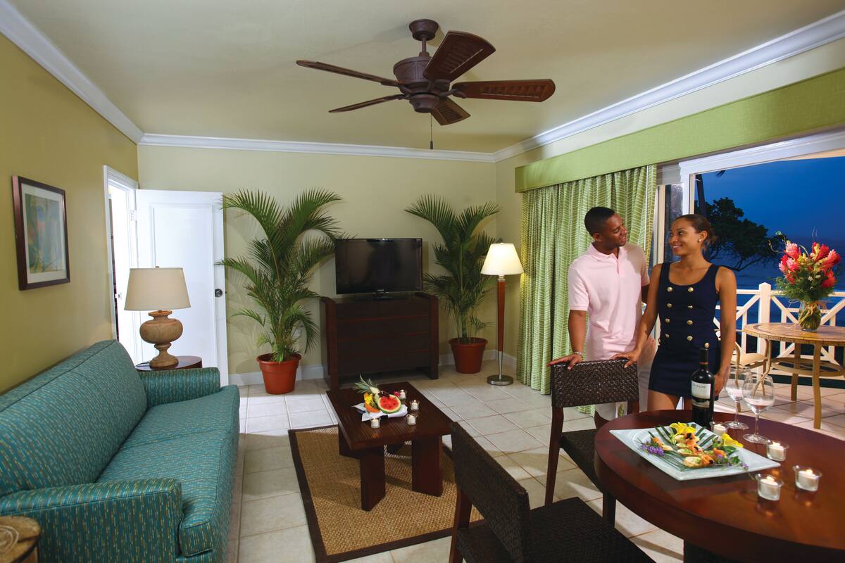 A living room with a sofa, a coffee table, a TV, and a dining area with a table set for two.