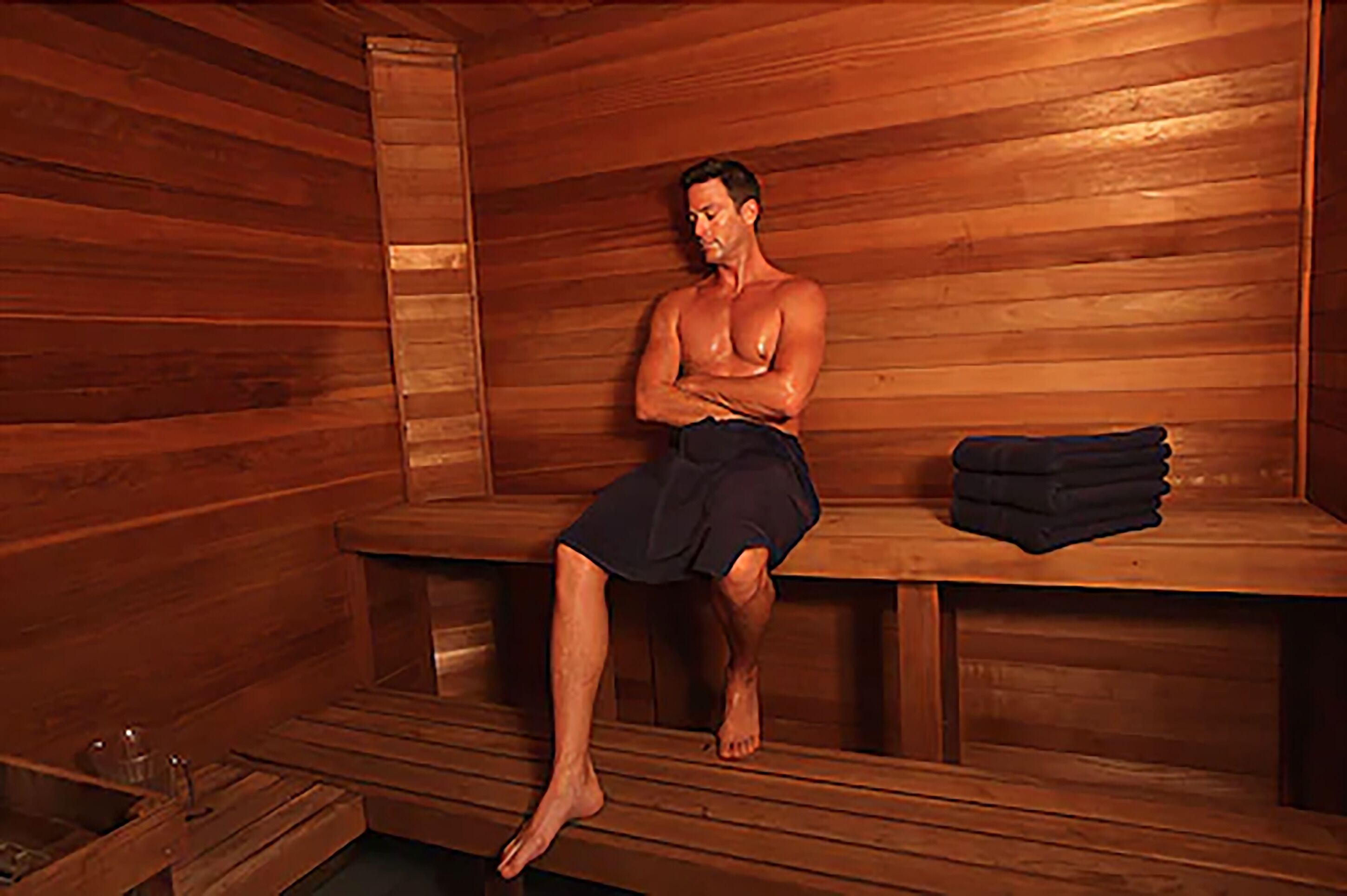 Una sauna con bancos de madera y un banco con una esterilla doblada.