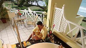 A person relaxing in a large bathtub filled with water and rose petals, with a view of the ocean and palm trees in the background. - Magdalena Grand Beach & Golf Resort (Lowlands)