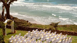 A beachside ceremony setup with rows of white chairs tied with yellow sashes, overlooking the ocean. - Magdalena Grand Beach & Golf Resort (Lowlands)