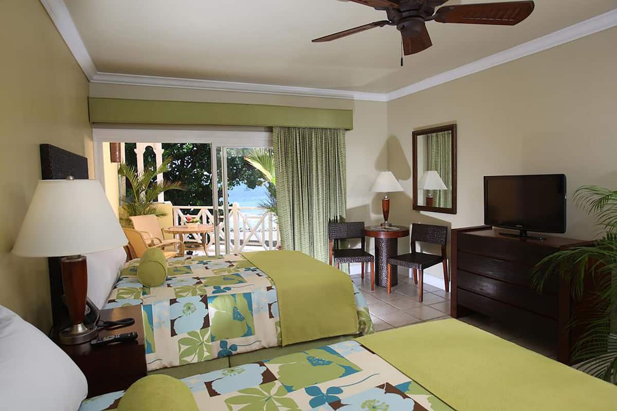 A hotel room with two beds, a TV, a desk, and a balcony with a view of the outdoors.