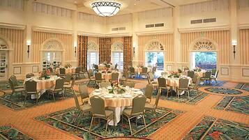 A large banquet hall with multiple round tables set for dining, high ceilings, and ornate chandeliers.
