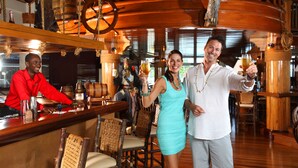 A bar area with wooden furniture, a bartender, and a couple holding drinks. - Magdalena Grand Beach & Golf Resort (Lowlands)