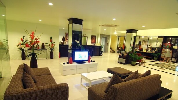 A modern living room with a flat-screen TV, brown sofas, a white coffee table, and decorative plants. - Laem Din Hotel Chaweng (Koh Samui)