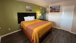 A hotel room with a bed, green walls, a painting, a lamp, and a door. - Executive Inn and Kitchenette Suites (Eagle Pass)
